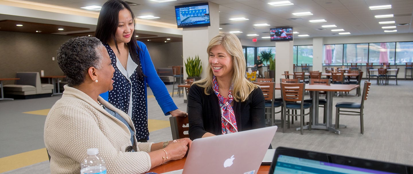 Three ladies having a conversation at a table while using a laptop at the Minnesota State University Edina campus